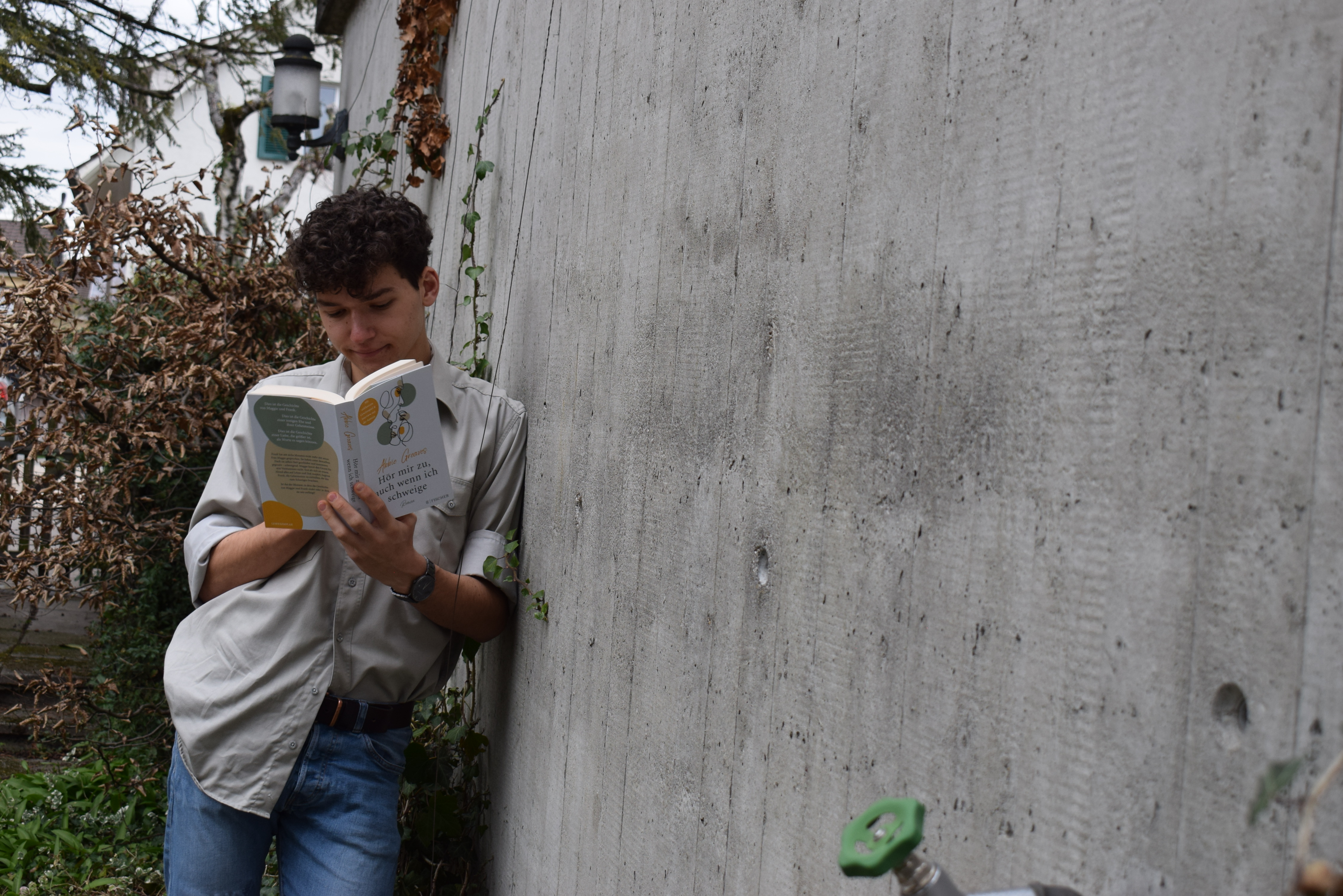 Josia Jourdan - cute young guy leaning against a wall reading the silent treatment - he wears a safari shirt and has curly crown hair - reading guy - young reading guy